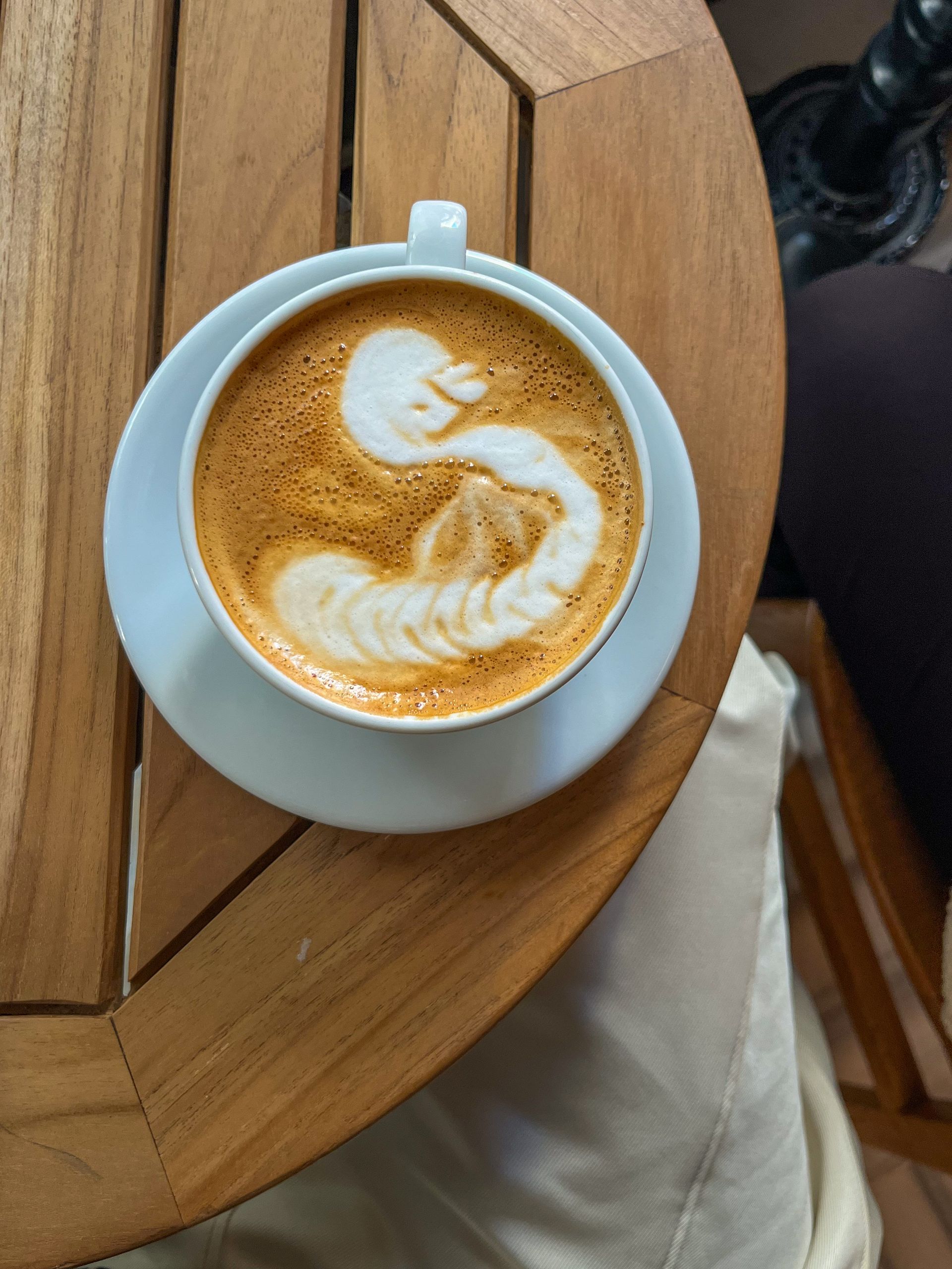 A latte with a swan poured into the foam, seen from above on a timber table