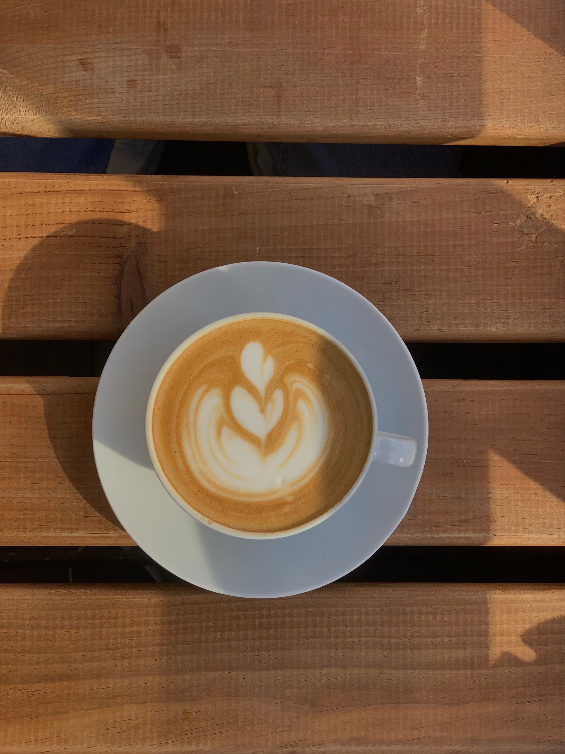 A latte on a sunlit outdoor table facing the foreshore